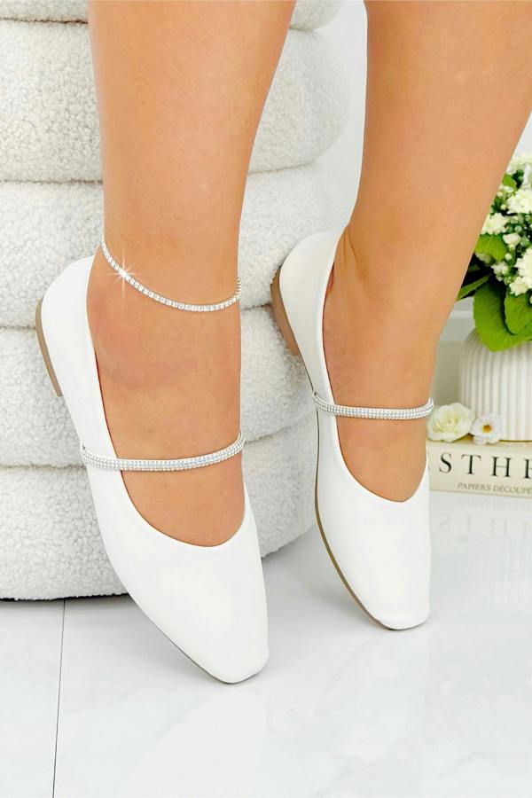 White ballerina shoes with ankle straps worn by a person on a light background