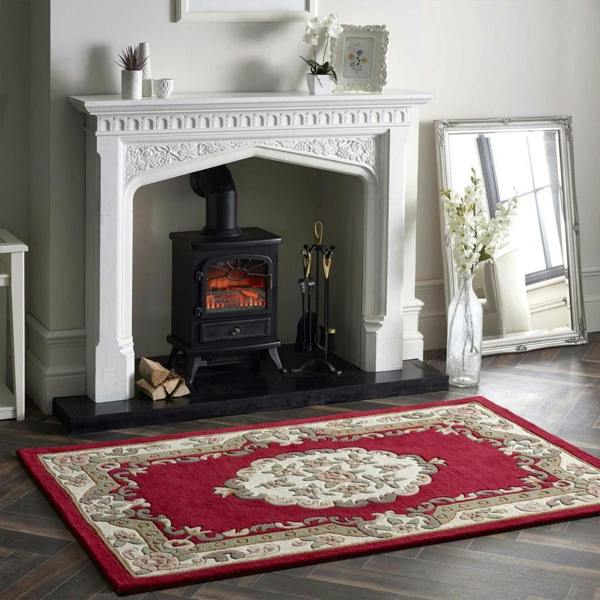 Decorative red rug with intricate patterns in front of a white fireplace.