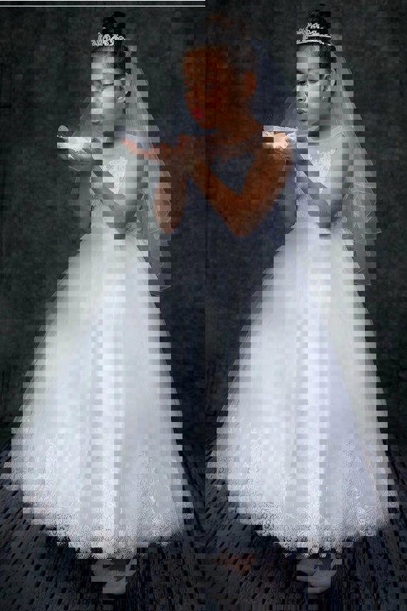 Young girl in a white lace dress blowing bubbles against a dark background