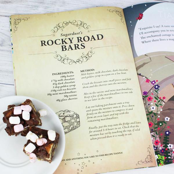 Open view of the Personalised Fairy Baking Adventure storybook featuring Sugardust's Rocky Road Bars recipe next to two real rocky road slices on a saucer