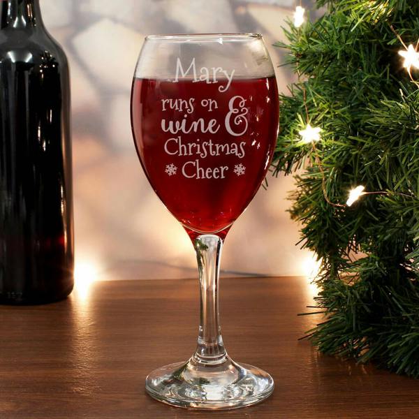 Personalised wine glass engraved with the name Mary and runs on wine and Christmas cheer filled with red wine beside a Christmas tree