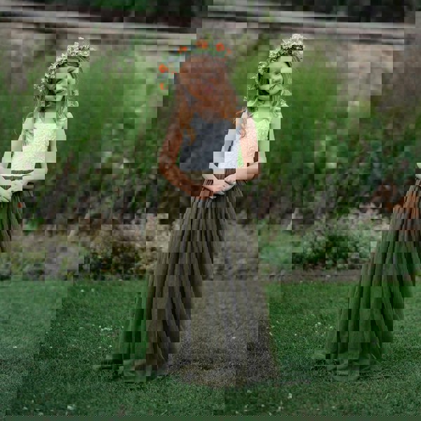 Young girl in a white top and green skirt with a flower crown standing in a grassy field.