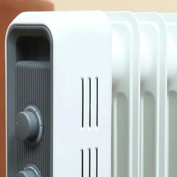 Close-up of white oil-filled radiator heater front vents and control knobs
