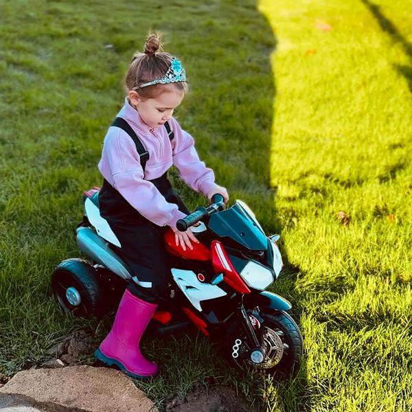 Child riding a kids electric motorcycle toy with red body, black seat, and front lights