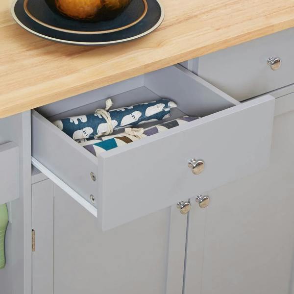 Grey kitchen cart drawer open with neatly folded cloths and utensils.