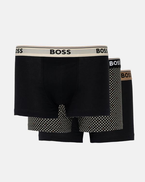 Three BOSS men's boxer briefs in black, arranged in a 3-pack. The front pair has a beige waistband with black BOSS lettering, while the pairs behind it feature black and white polka-dot patterns on the legs and a brown BOSS logo on their waistbands.