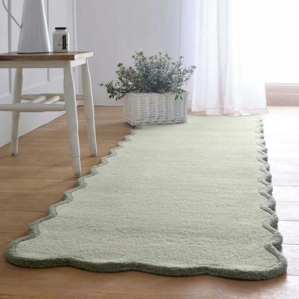 Green runner rug on a wooden floor with a white stool and plant in the background.