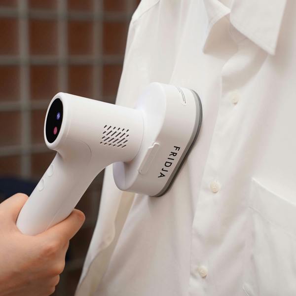 A person uses the Fridja f20 Handheld Clothes Steamer Pro with Suction to effortlessly remove wrinkles from a white button-up shirt, demonstrating the convenience of this portable iron alternative.