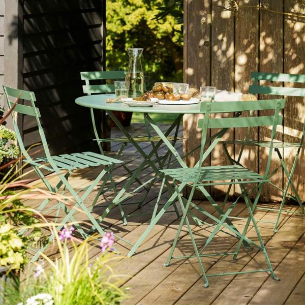 Four-seater thistle green metal folding bistro table and chairs set styled with a carafe and platter on a wooden garden deck.