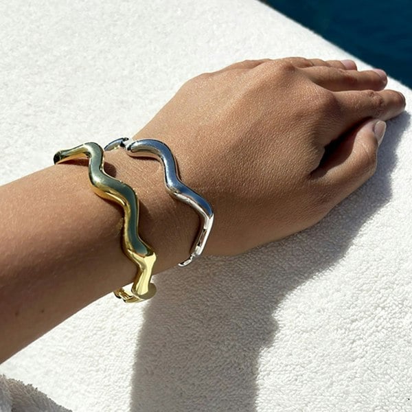 A close up of a hand and wrist showcasing gold vermeil and silver cuffs.