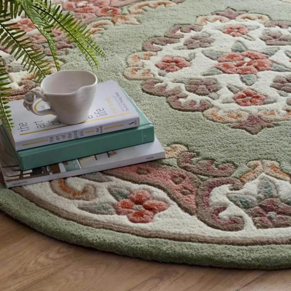 Decorative round rug with floral patterns on a wooden floor, featuring a cup and books.