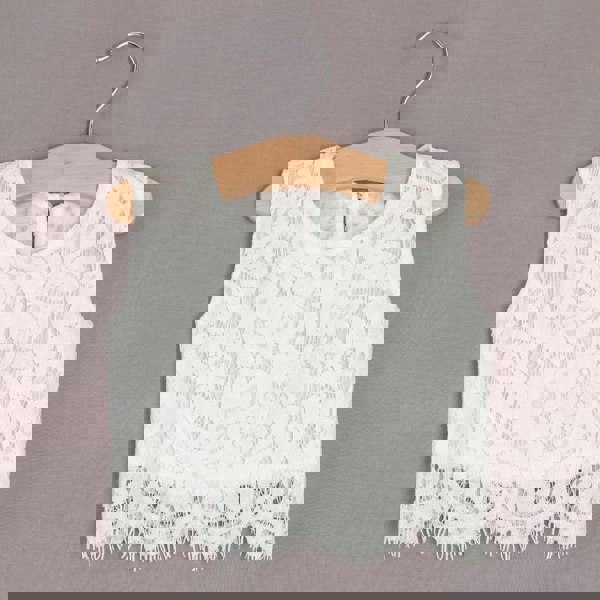 White lace top on a wooden hanger against a grey background