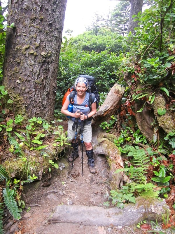 Person hiking through a lush forest with backpack and walking sticks wearing a Ruffnek hiking snood scarf as a head / hair band. 
#HikingGear #HikingAdventures #HikingClothing #TravelScarf #MountainSnood