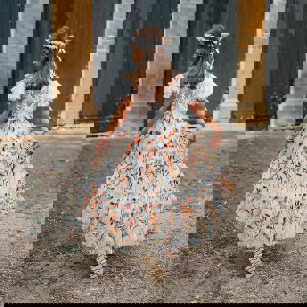 Girl in a floral dress walking away from the camera in front of a brick building.