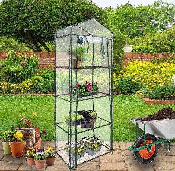 Mini greenhouse with four tiers, clear plastic cover, and sturdy metal frame, set in a vibrant garden with potted plants and a wheelbarrow