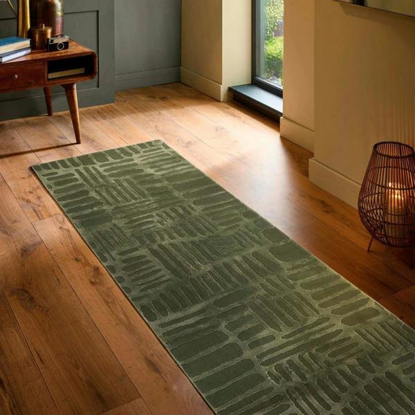 Green patterned rug on a wooden floor in a room with a lamp and books.