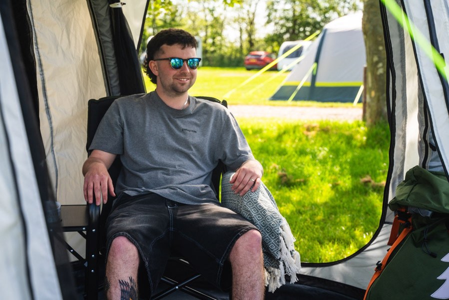 A man sits inside the Loopo Breeze® XL v2 Motorhome Awning by OLPRO, he is sat in a camping chair