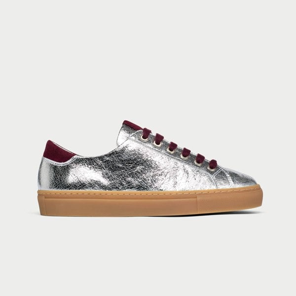 Silver sneaker with burgundy laces and sole on a light gray background
