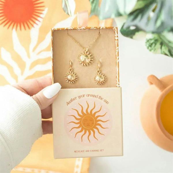 Sun-themed necklace and earring set with gold-tone sunburst charms on card