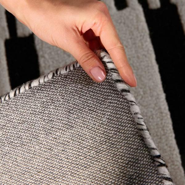 Hand holding a textured gray fabric with a patterned edge
