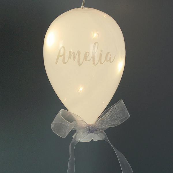 A lit frosted white glass balloon ornament personalised with the script name Amelia.