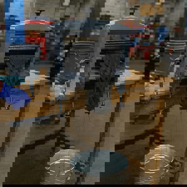 Manual hand wringer with a gray metal frame, squeezing water from a black cloth, positioned over a metal bucket on a wooden table