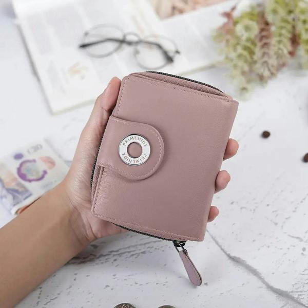 Hand holding a pink wallet with a decorative button on a light surface.