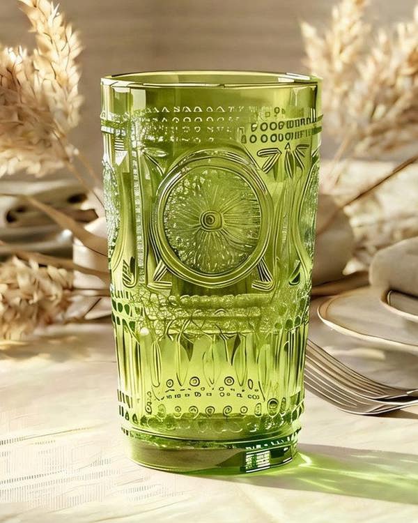 Two green textured glass tumblers on a white surface with a light wooden background.