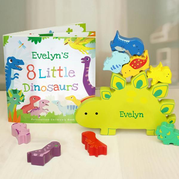 A personalised copy of Evelyn's 8 Little Dinosaurs storybook from Abode Home & Gifts, standing open next to a matching lime green wooden stegosaurus toy engraved with the name Evelyn, holding a stacked tower of smaller colourful wooden dinosaurs.