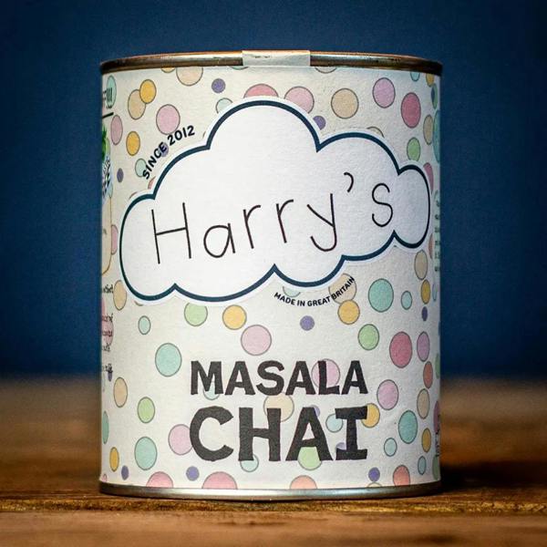 Recyclable polka-dot tin of Harry's Masala Chai tea handcrafted in Great Britain, resting on a rustic wooden table.
