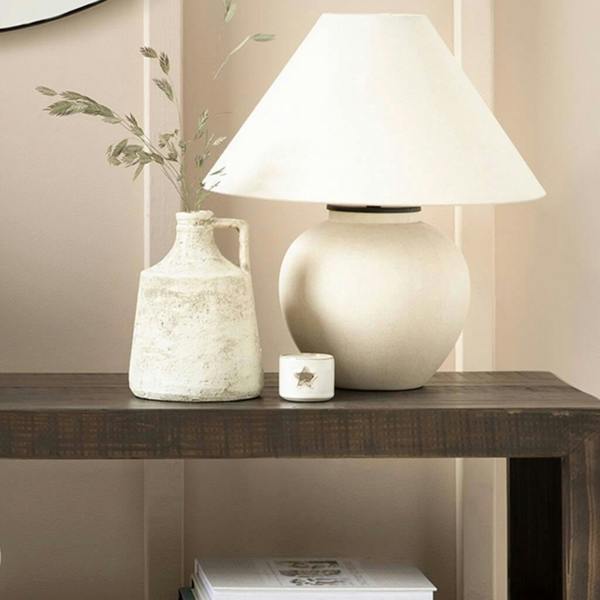 Ceramic table lamp with a wide natural fabric shade styled next to a rustic stoneware jug on a dark wood table.