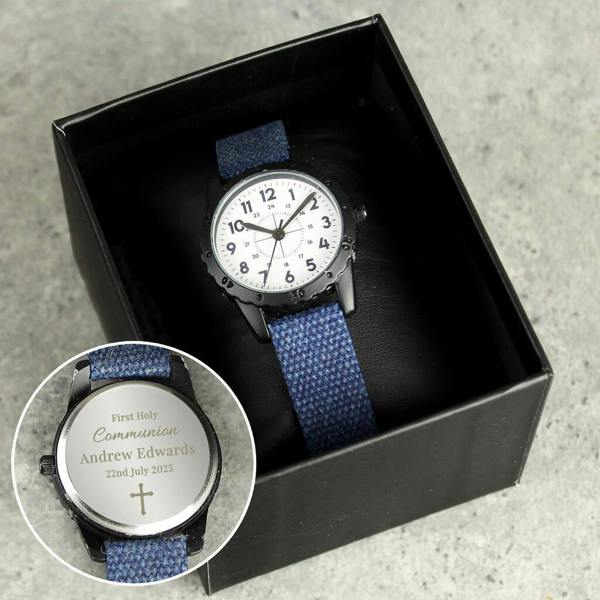 A Personalised First Holy Communion Watch with a blue canvas strap sitting in a black box, with a circular cutout showing the engraved caseback for Andrew Edwards.