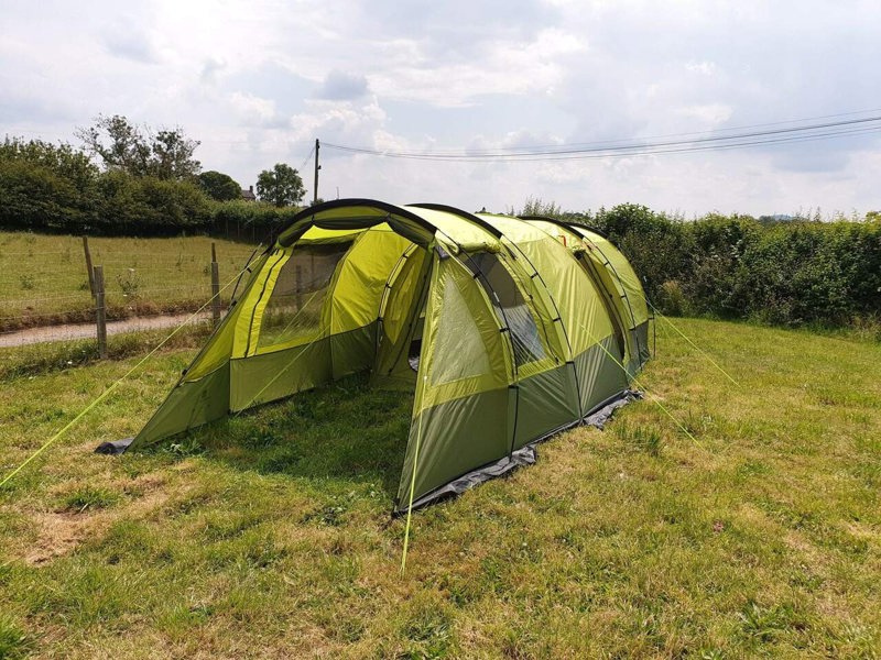 An image of the Abberley XL Extension by Olpro attached to the Abberley XL Tunnel Tent on a camping field with the front open and window blind open.