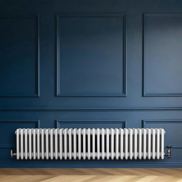 Traditional white 4 column radiator with valves, featuring a sleek design against a deep blue wall and wooden floor