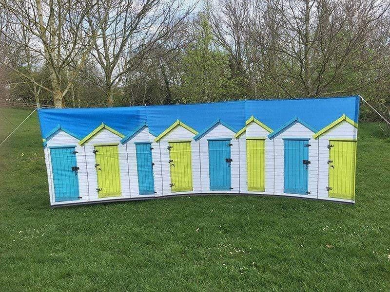 Beach Huts Design 4 Pole Compact Windbreak Steel Poles by OLPRO pictured on a field. It's Blue sky with White Beach huts with alternate blue and yellow doors fully assembled in a U shape.