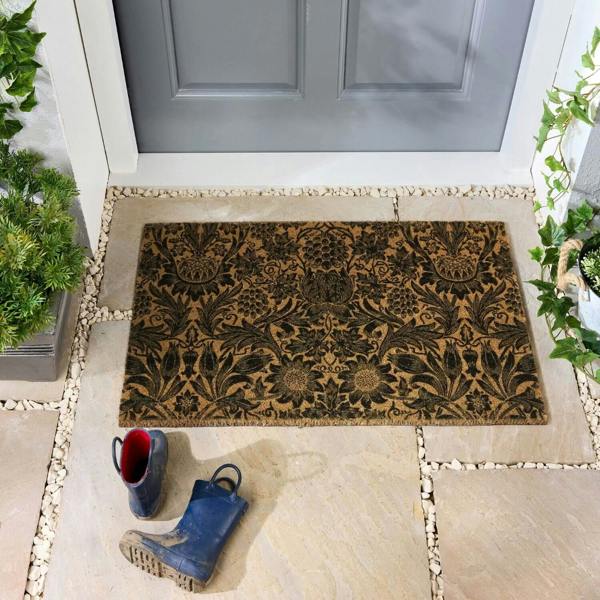 Decorative doormat with floral pattern on a stone patio in front of a gray door.