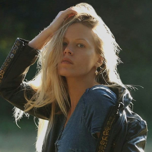 A blonde woman photographed in nature looking cool in denim and leather jacket.