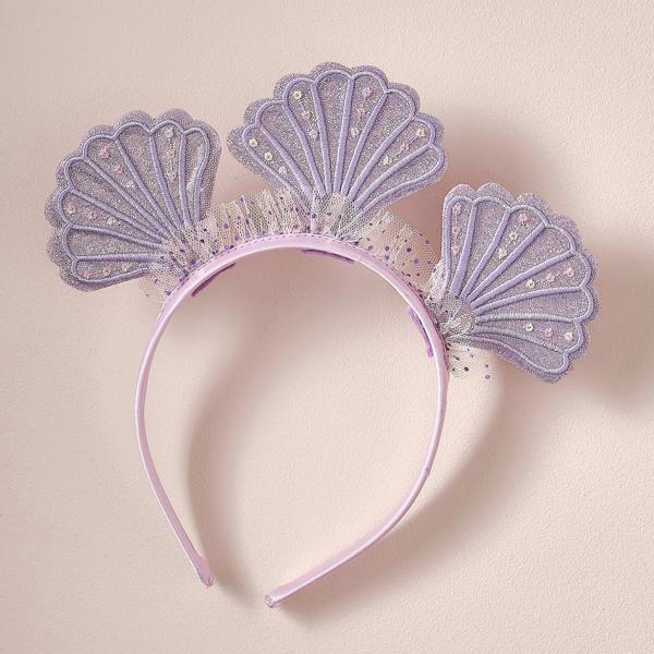 Purple satin children's mermaid headband with three glittery embroidered seashells and dotty tulle ruffles against a pink background.