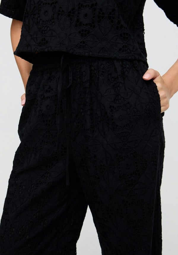 Person wearing a black textured outfit with wide-leg pants and a cropped top on a light gray background