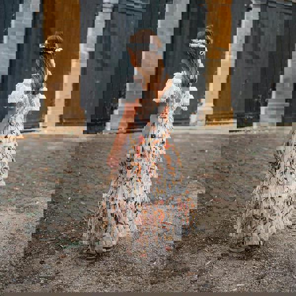 Girl  in a floral dress standing in front of a brick building with arched doors.