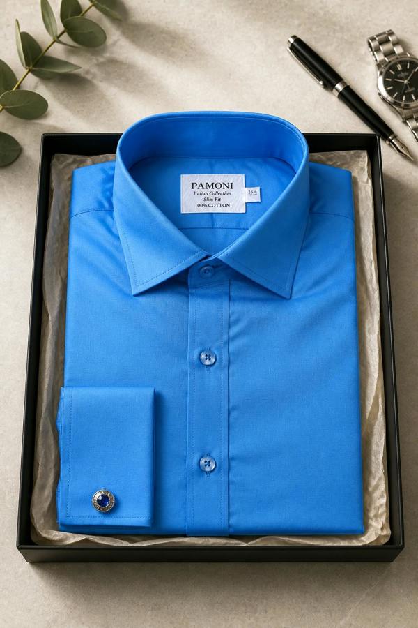 Blue dress shirt in a box with 'Pamoni' label, surrounded by a pen, watch, and leaves on a beige surface.