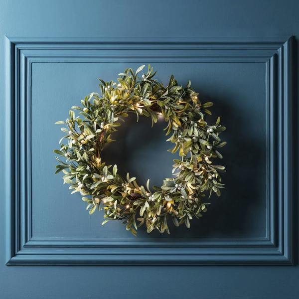 As featured in House Beautiful: 50cm pre-lit mistletoe artificial Christmas wreath with 50 warm white micro LEDs, hanging on a dark blue panelled wall.