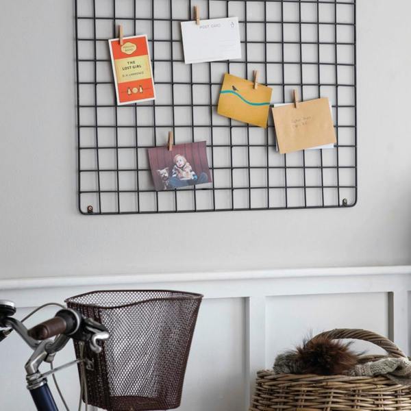 A large wire memo board mounted landscape on a grey wall above a bicycle and wicker basket.