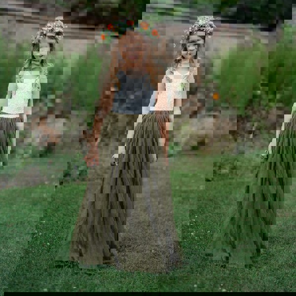 Young girl in a white top and green skirt standing in a garden.