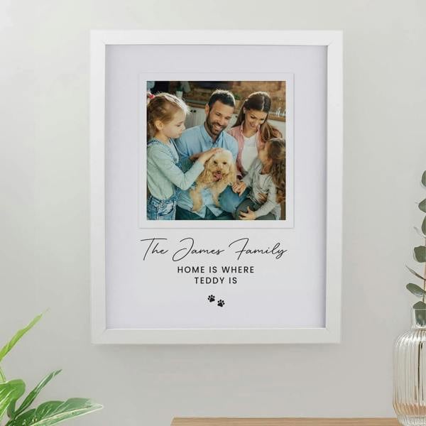 A white framed print displaying a family photo with a golden dog, customized with text reading The James Family Home is Where Teddy Is and paw prints.