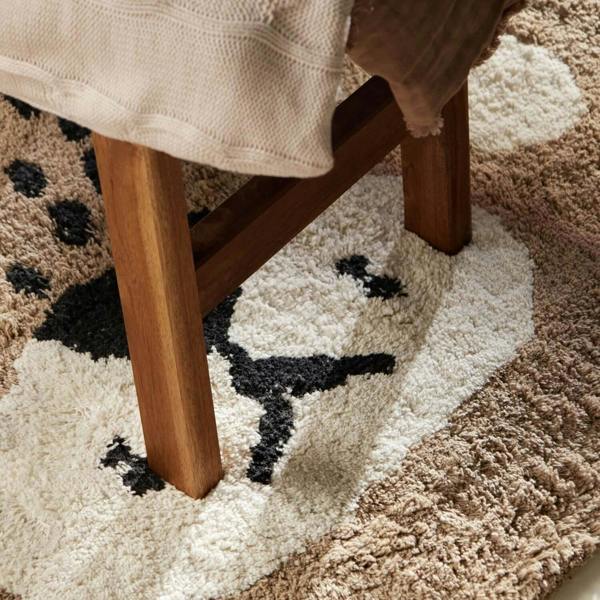 Close-up of a wooden stool on a patterned rug with a blanket draped over it.