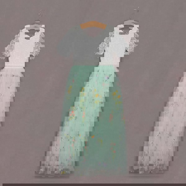 White top with lace sleeves and a light green skirt with floral embroidery on a hanger against a gray background.