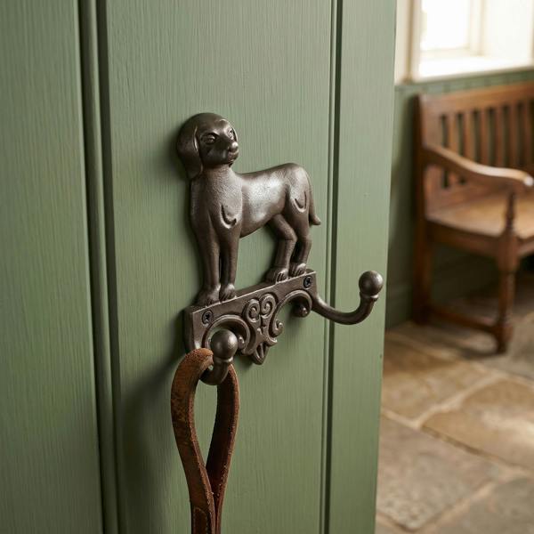 Antique cast iron twin coat hook with intricate dog design mounted in a vintage home entryway, highlighted by warm lighting and rustic charm.