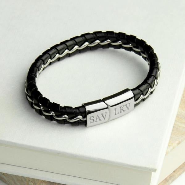 A black braided genuine leather men's bracelet with silver metal details and an engraved clasp showing initials SAV and LKV, resting on a white book.