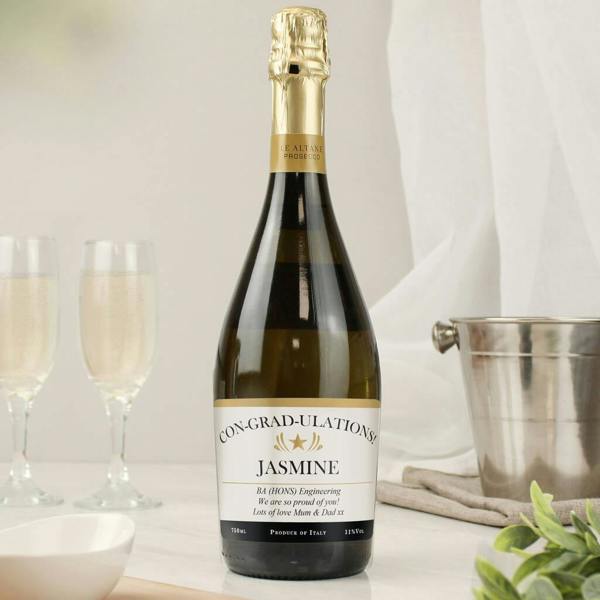 A 75cl bottle of personalised classic Italian Prosecco with a custom graduation label next to two filled champagne flutes on a marble surface.